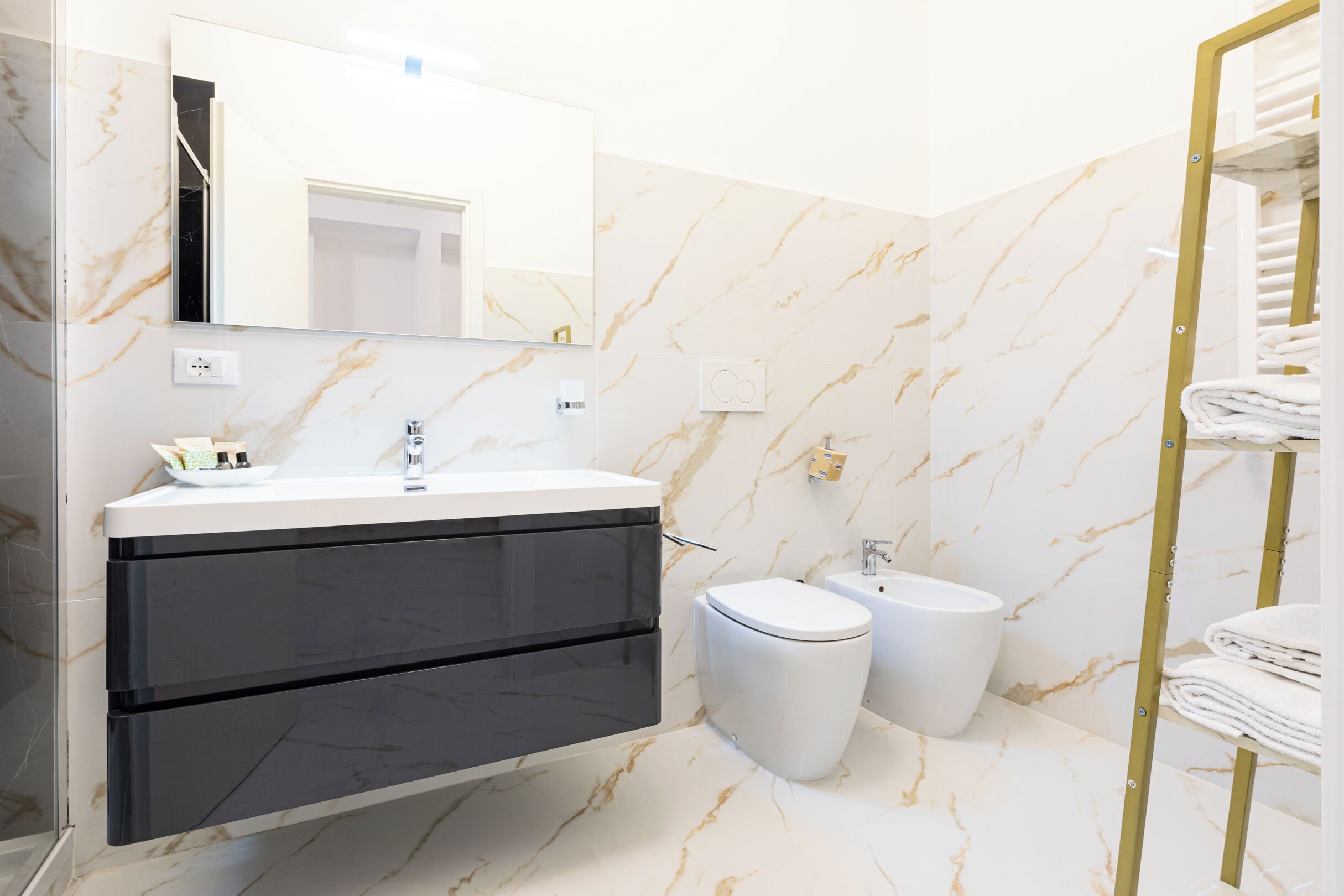 Une salle de bain moderne avec un sol en marbre, un lavabo blanc, un meuble noir, des toilettes et un porte-serviettes.