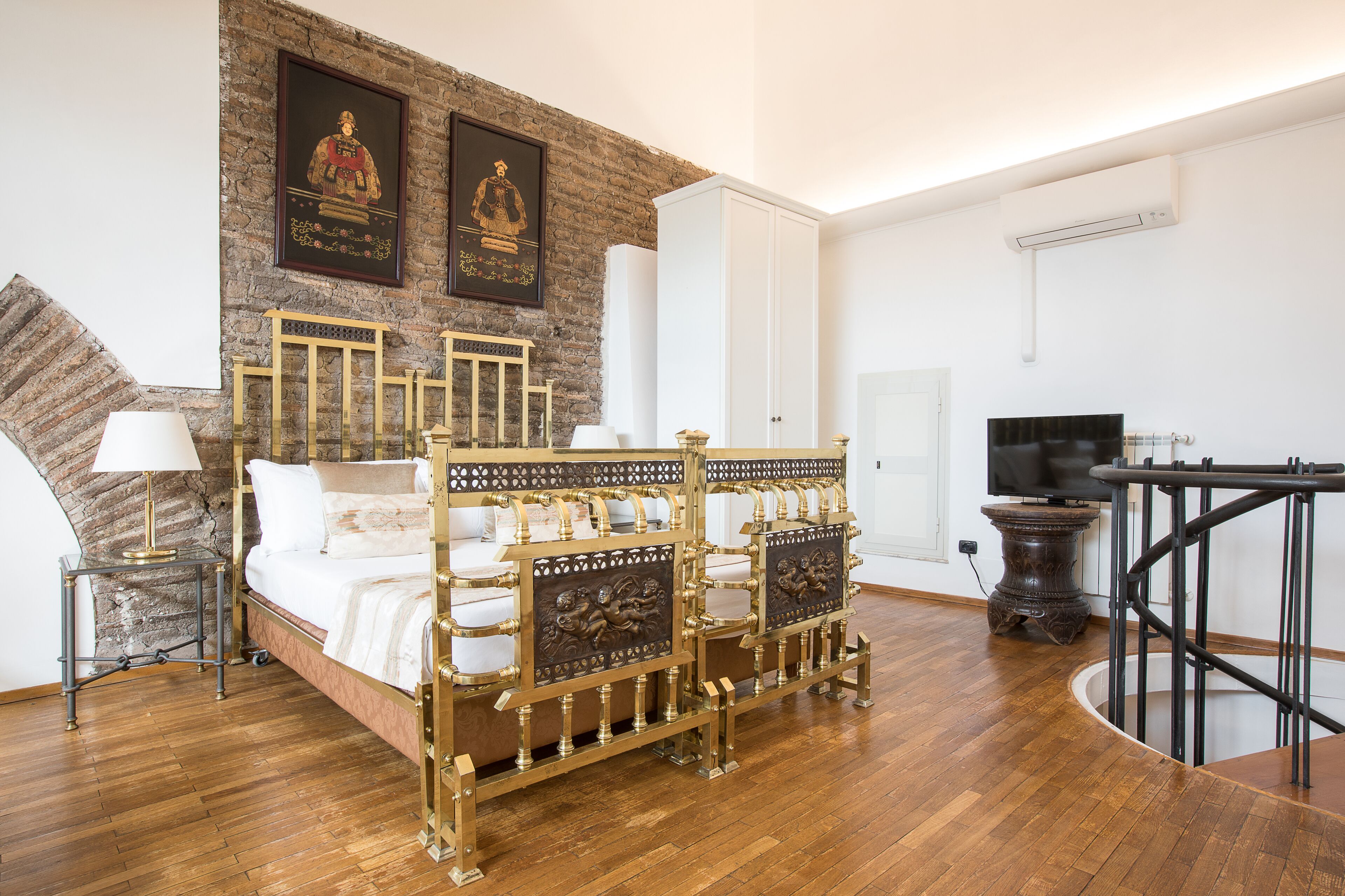 Una camera da letto con pavimento in legno, un letto con testiere elaborate, una TV e una scala.