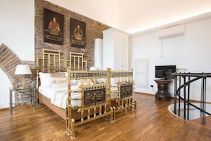 Une chambre avec un plancher en bois, un lit doté d’une tête de lit décorée, une télévision et un escalier.