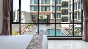 A hotel room with a large window overlooking a swimming pool and a building with multiple floors. - Beston Pattaya (Pattaya)