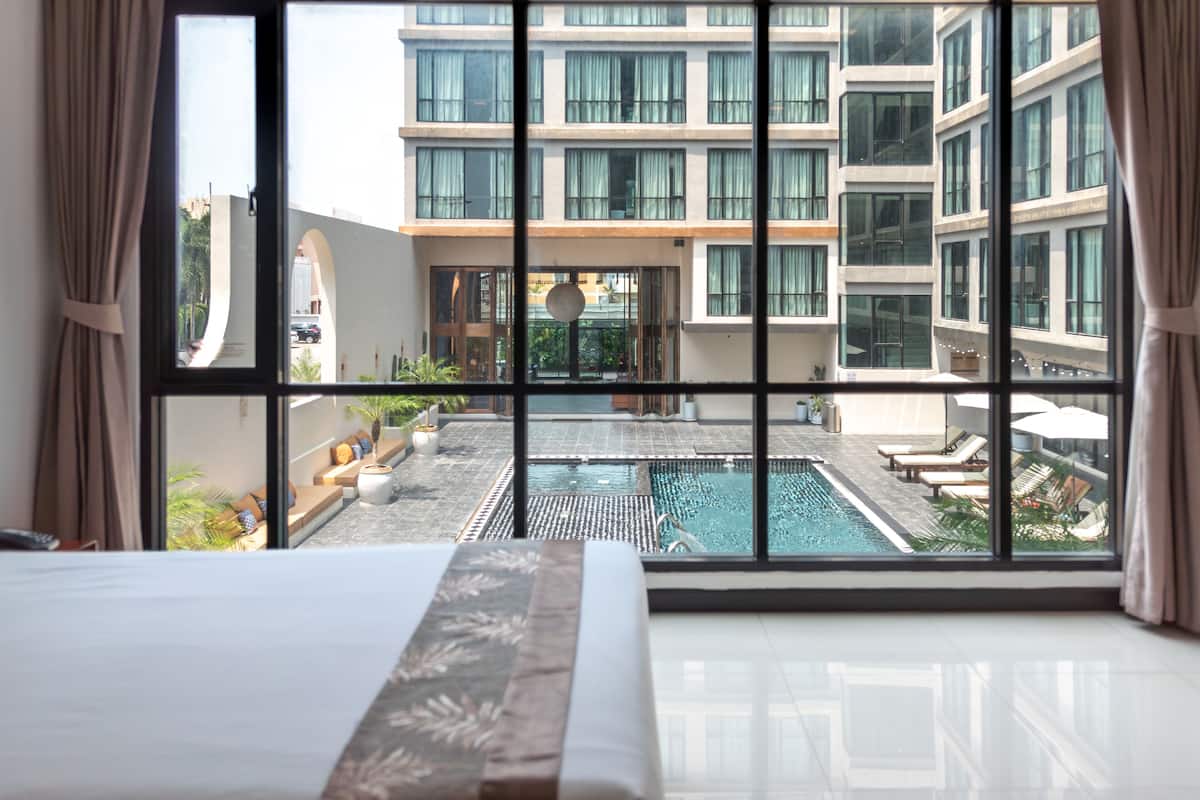 A hotel room with a large window overlooking a swimming pool and a building with multiple floors.