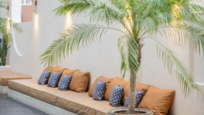 A modern outdoor seating area with a sofa and cushions, surrounded by palm trees and a white wall with a large arch window. - Beston Pattaya (Pattaya)