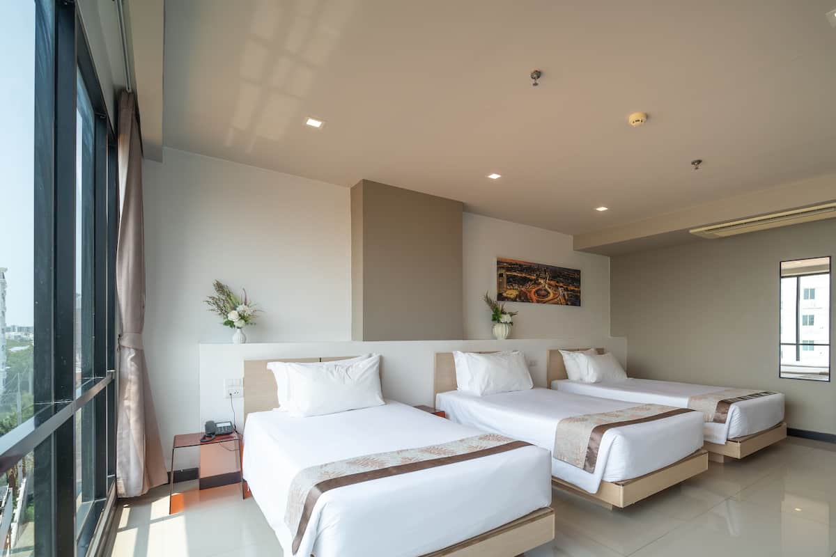 A modern hotel room with three beds, a large window, and a city view.
