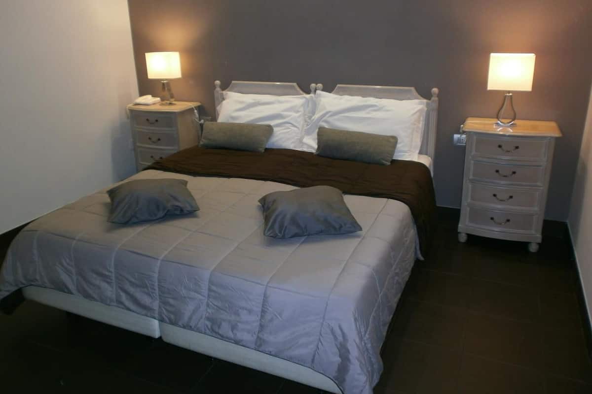 A neatly made bed with a grey comforter and pillows, flanked by two bedside tables with lamps.