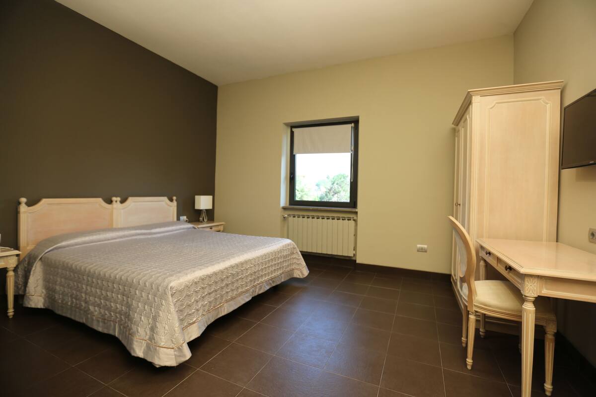 A bedroom with a bed, a desk, a chair, a window, and a radiator.