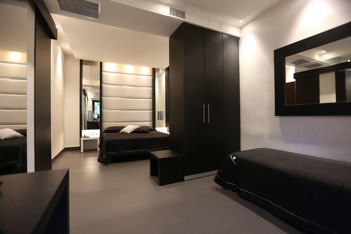 A modern bedroom with a large bed, a wardrobe, a bedside table, and a mirror on the wall.