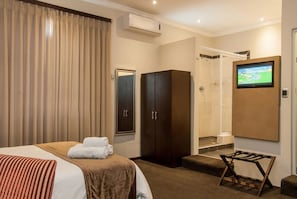 A hotel room with a bed, a wardrobe, a shower area, and a TV mounted on the wall.