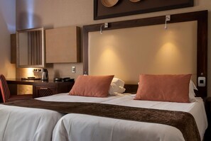 Habitación de hotel con una cama grande, un escritorio con silla, un espejo y una lámpara fijada a la pared.