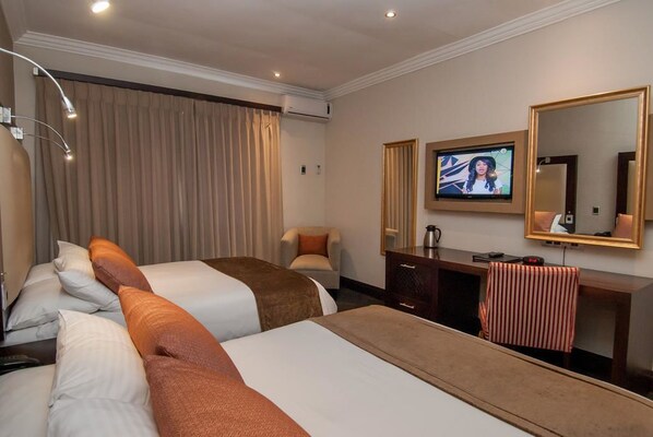 Habitación de hotel con dos camas, un escritorio, una silla, un televisor y un espejo grande.