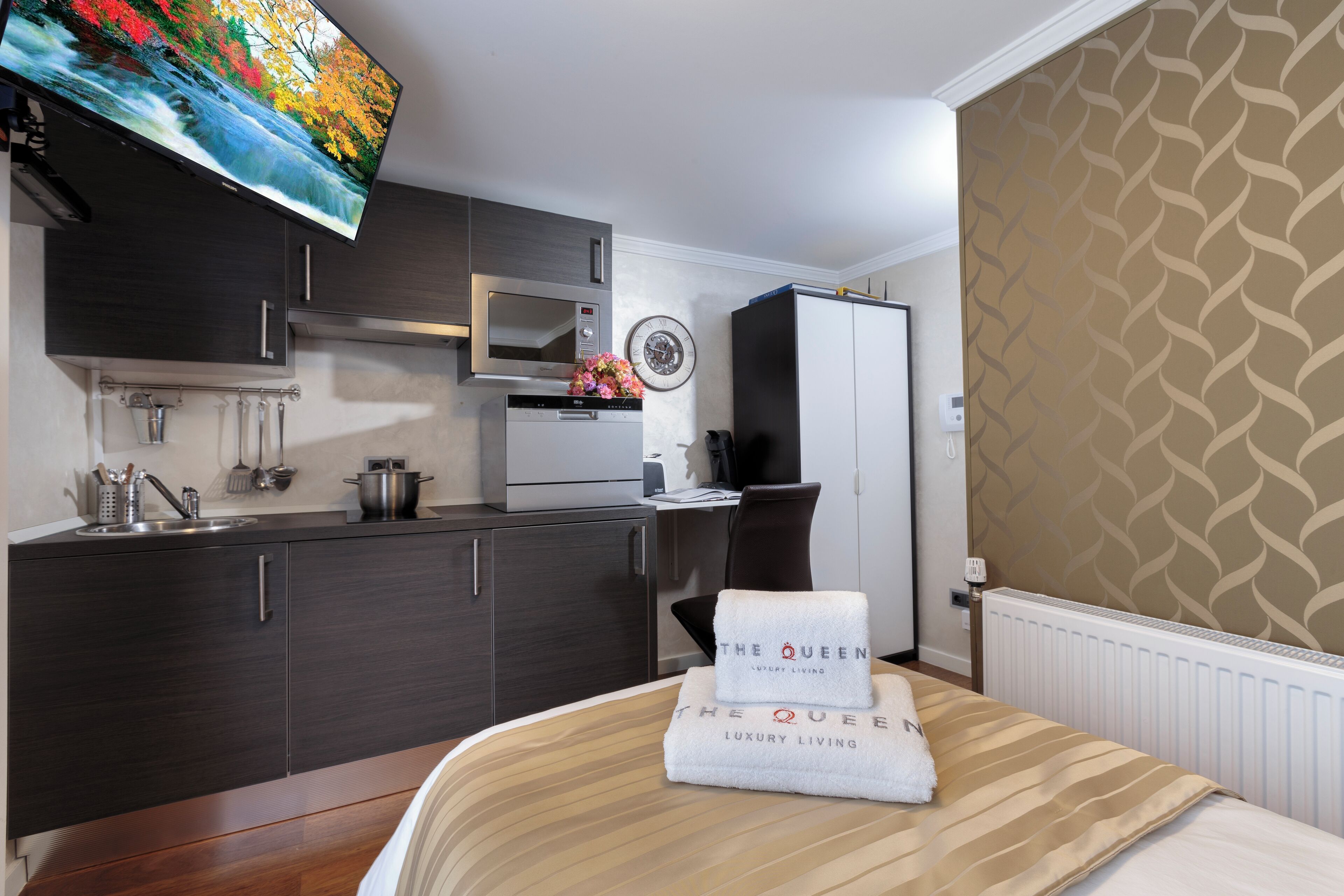Una habitación de hotel pequeña con kitchenette, una cama y una toalla de la marca, además de un televisor montado en la pared.