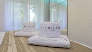 A hotel room with a bed, two towels with "The Queen Luxury Living" branding, and sheer curtains. - The Queen Luxury Apartments Villa Vinicia (Luxembourg City)