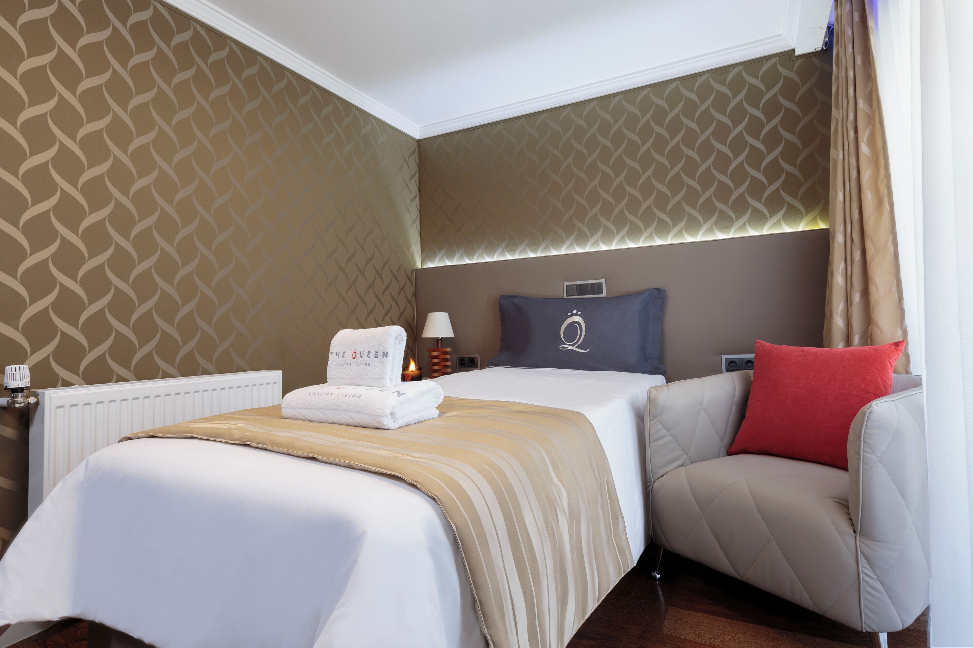 Ein Hotelzimmer mit einem Bett, einem Sessel, einem Nachttisch, einer Lampe und einer Wand mit geometrischem Muster.