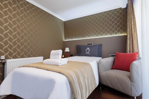 Habitación de hotel con cama, una silla, mesita de noche, lámpara y pared con diseño geométrico.