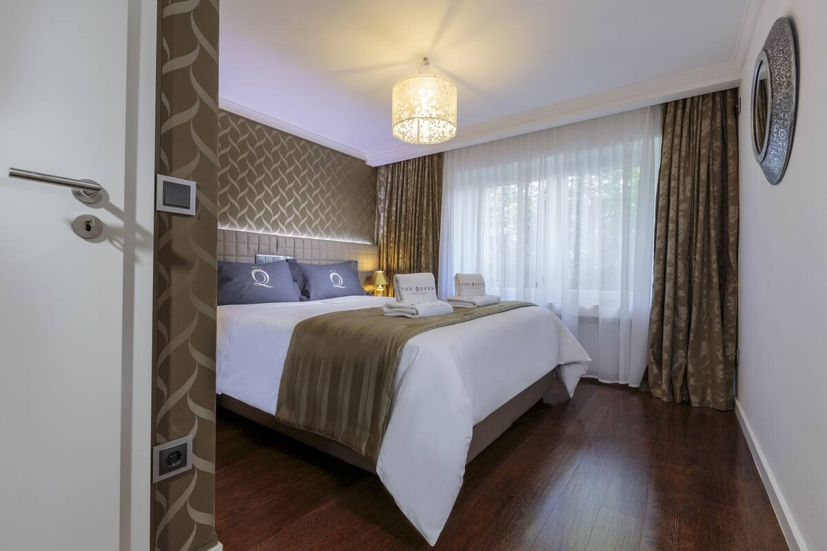 A hotel room with a bed, a bedside table, a lamp, and a window with curtains.