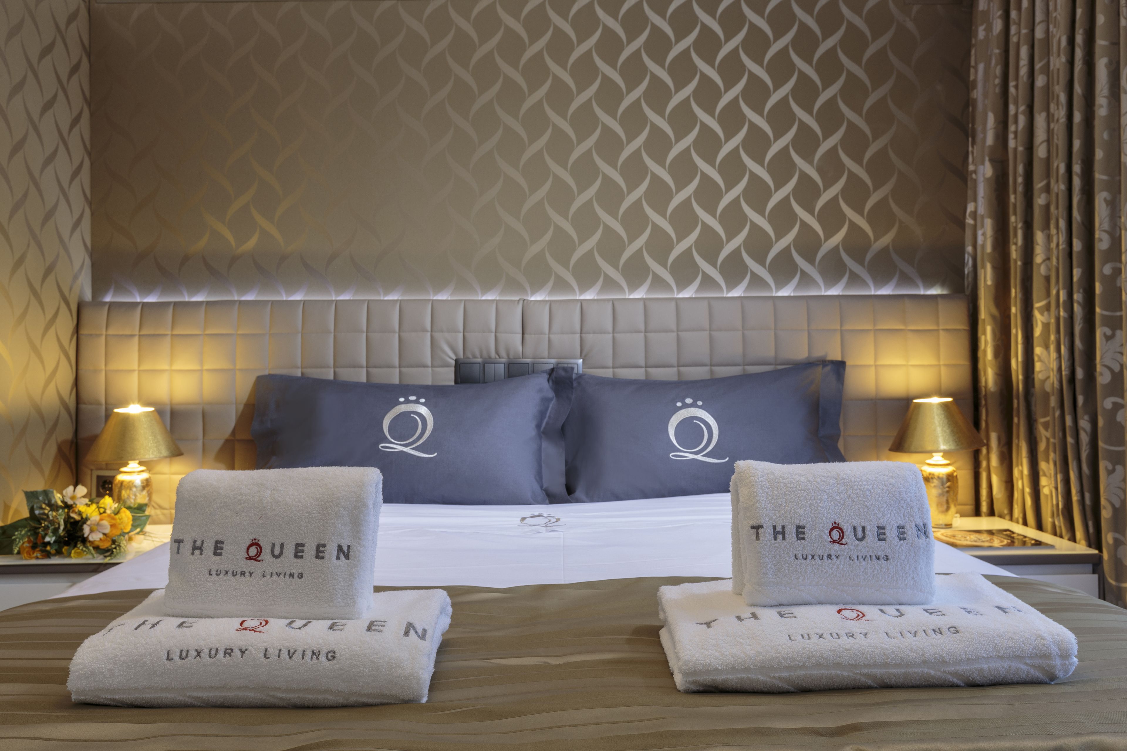 A hotel room with a large bed, two pillows with a crest logo, bedside lamps, and two towels with the hotel name.
