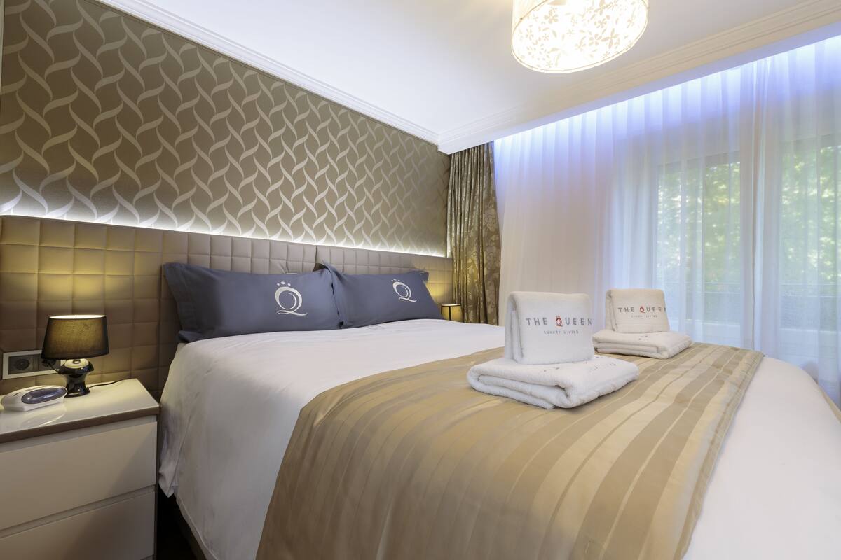 A hotel room with a large bed, a headboard with a geometric pattern, a bedside lamp, and a window with curtains.