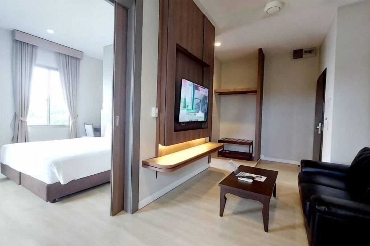 Quarto de hotel com cama, televisão na parede, mesa de centro e sofá.