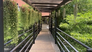 A covered walkway with metal railings, surrounded by lush greenery and plants. - J Park Hotel (Chonburi)