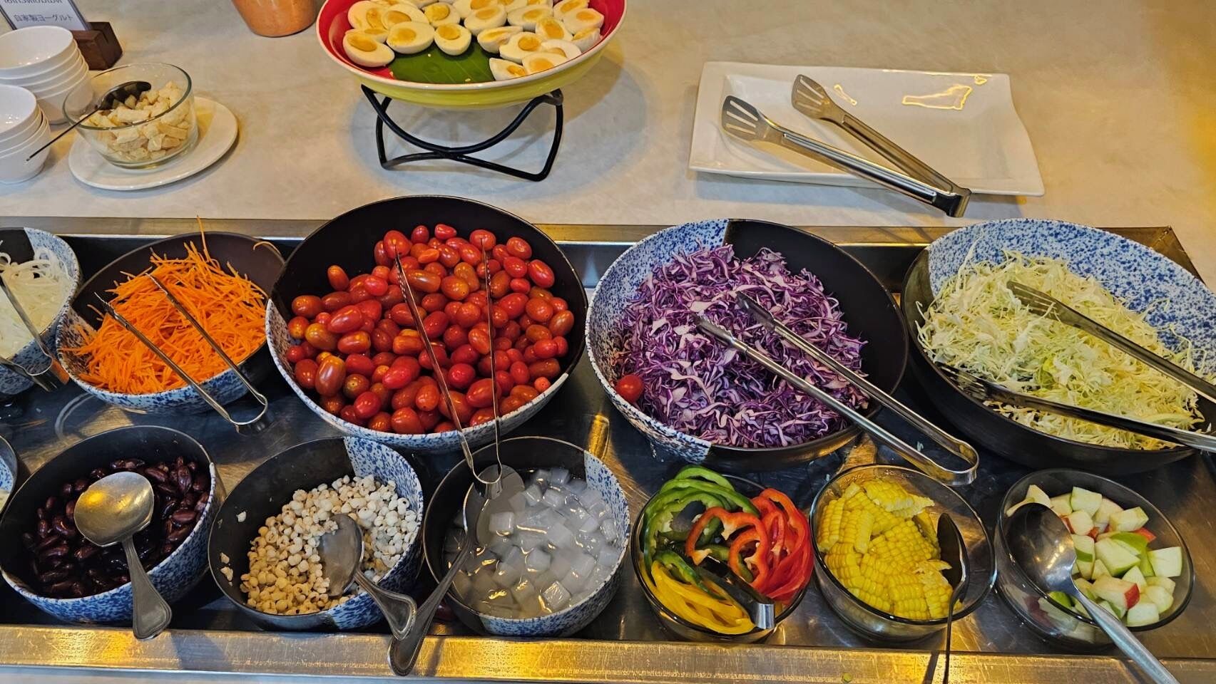 A buffet with various food items including eggs, carrots, tomatoes, cabbage, and corn.