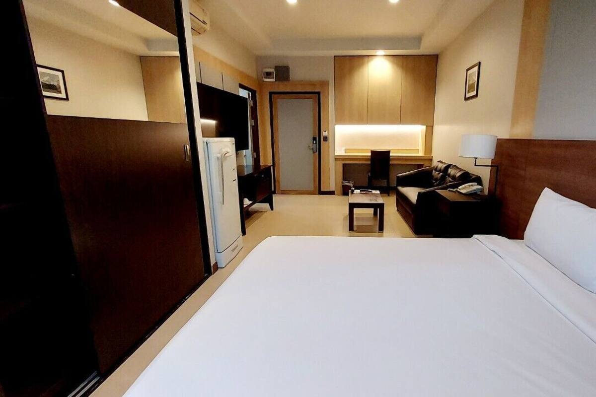 Quarto de hotel com uma cama grande, uma escrivaninha com cadeira, televisão e guarda-roupa.