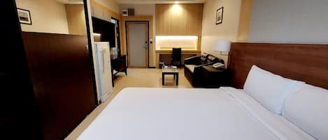A hotel room with a large bed, a desk with a chair, a TV, and a wardrobe.
