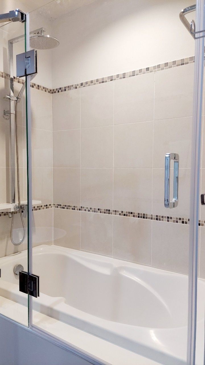 Un baño con ducha envuelta en vidrio, bañera y pared de azulejos con un detalle decorativo.