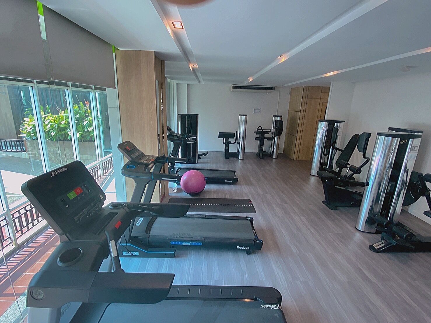 Uma academia com esteiras, um elíptico Reebok e uma bola de exercício rosa.