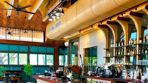 A bar area with a long counter, bar stools, and a variety of bottles on shelves. - J Park Hotel (Chonburi)