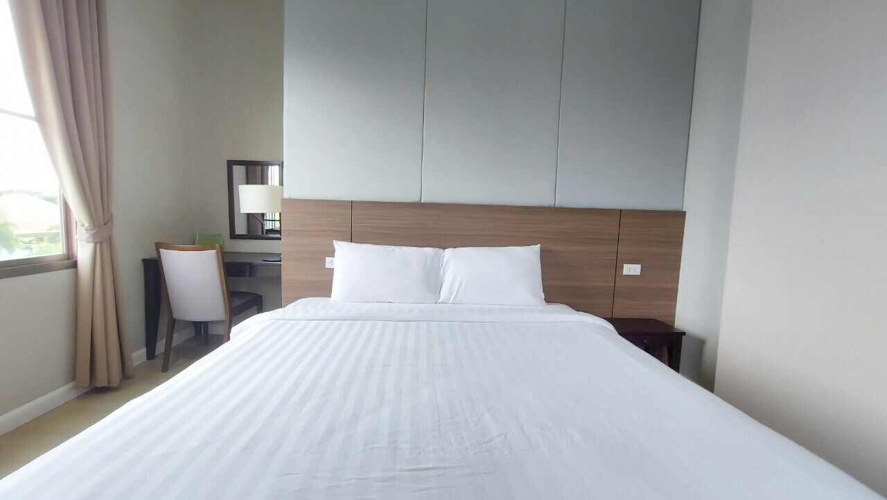 Una habitación de hotel con una cama grande, un escritorio con una silla, un espejo y una ventana con cortinas.