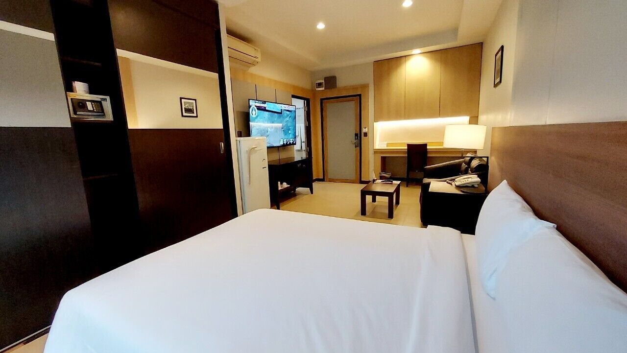 Hotellihuone, jossa on suuri sänky, työpöytä tuolilla, televisio ja minibaari.