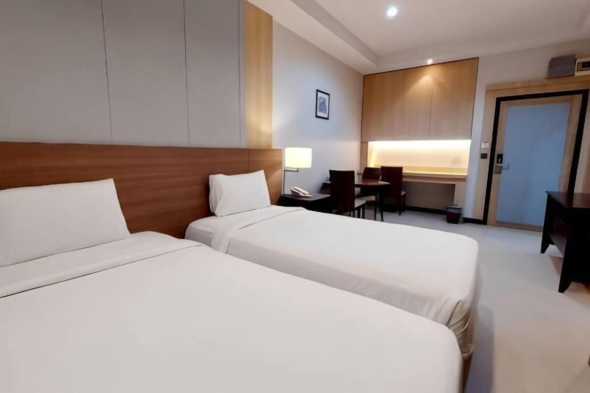 Quarto de hotel com duas camas, uma escrivaninha, uma cadeira e uma mesa pequena.