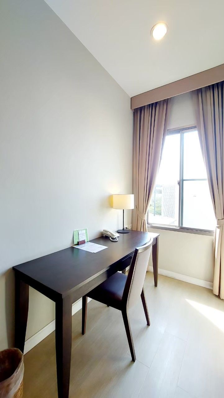 A hotel room with a desk, chair, lamp, and a window with curtains.