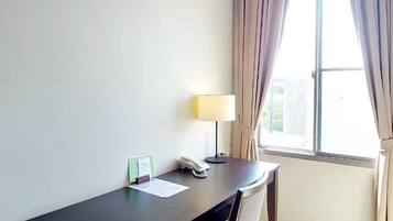 A hotel room with a desk, chair, lamp, and a window with curtains.