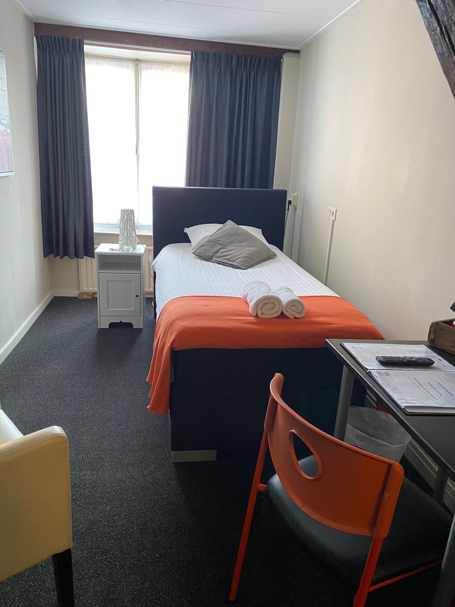 Ein Hotelzimmer mit Bett, Schreibtisch, Stuhl und einem fenster mit Vorhängen.