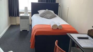 Ein Hotelzimmer mit Bett, Schreibtisch, Stuhl und einem fenster mit Vorhängen.
