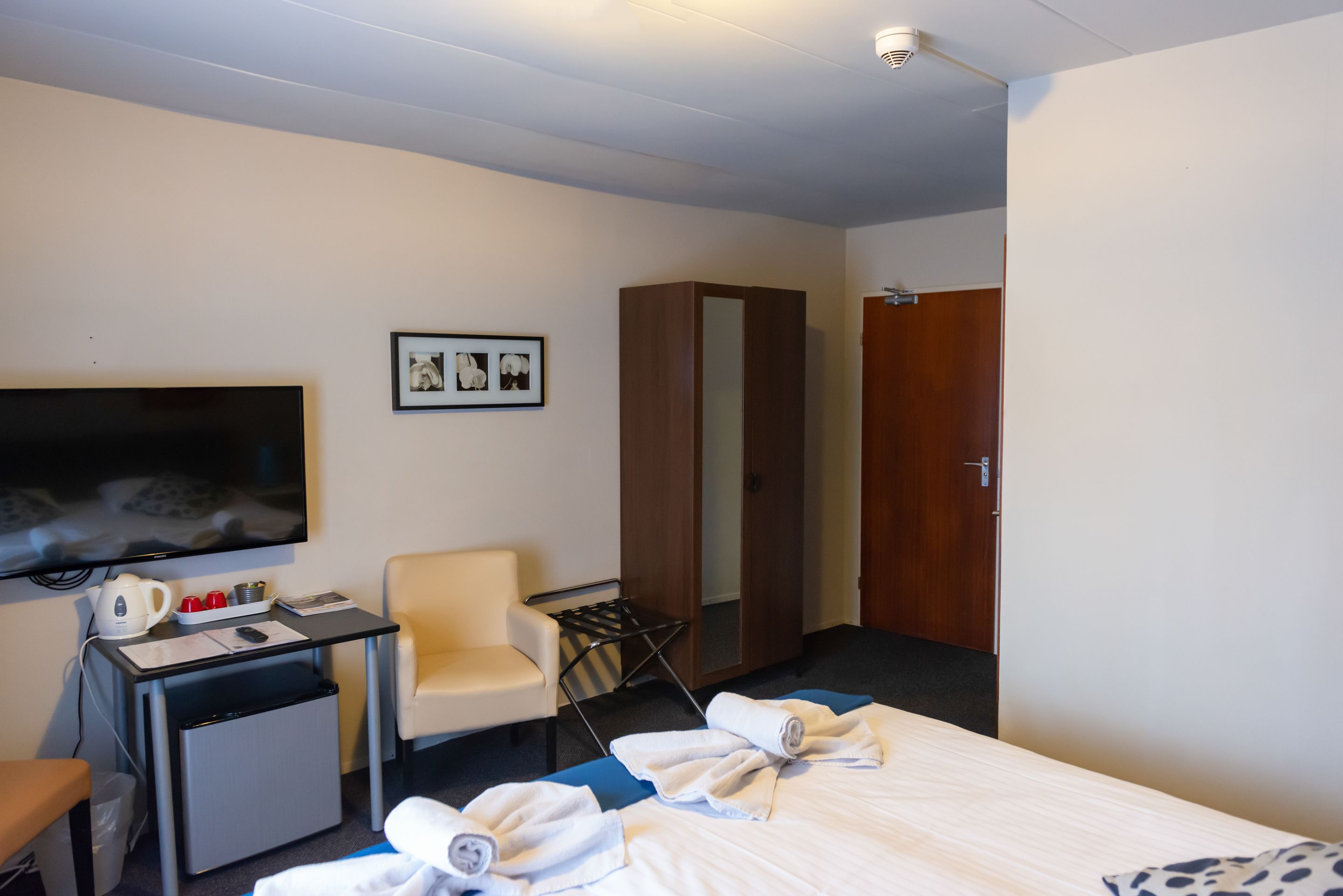 Une chambre d’hôtel comprenant un lit, un bureau avec une bouilloire, une chaise, une armoire et un téléviseur.