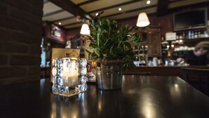A bar setting with a metal bucket containing a plant, a candle, and a glass of ice cubes on a dark wooden table. - Hotel en Grand Café de Pauw (Roermond)