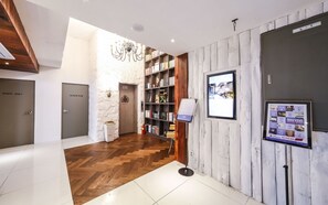 A hotel lobby with a wooden floor, a reception desk, a bookshelf, and a wall-mounted TV. - February Hotel - Busan Songdo (Busan)