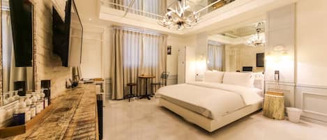 A modern hotel room with a large bed, a vanity with toiletries, a chandelier, and a large mirror.