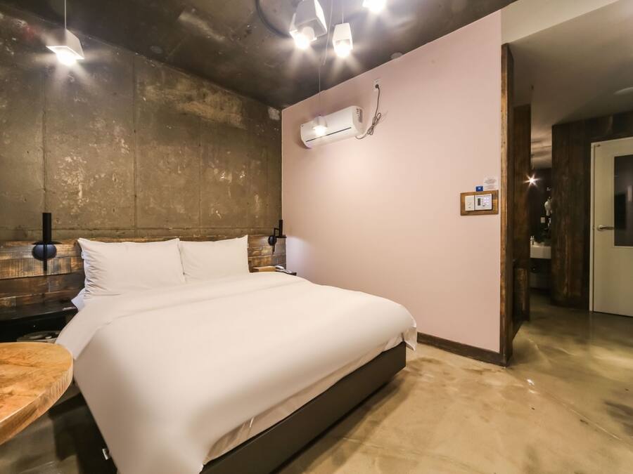 Una habitación de hotel moderna con una cama grande, cabecera de madera, una mesa redonda de madera y un equipo de aire acondicionado integrado.