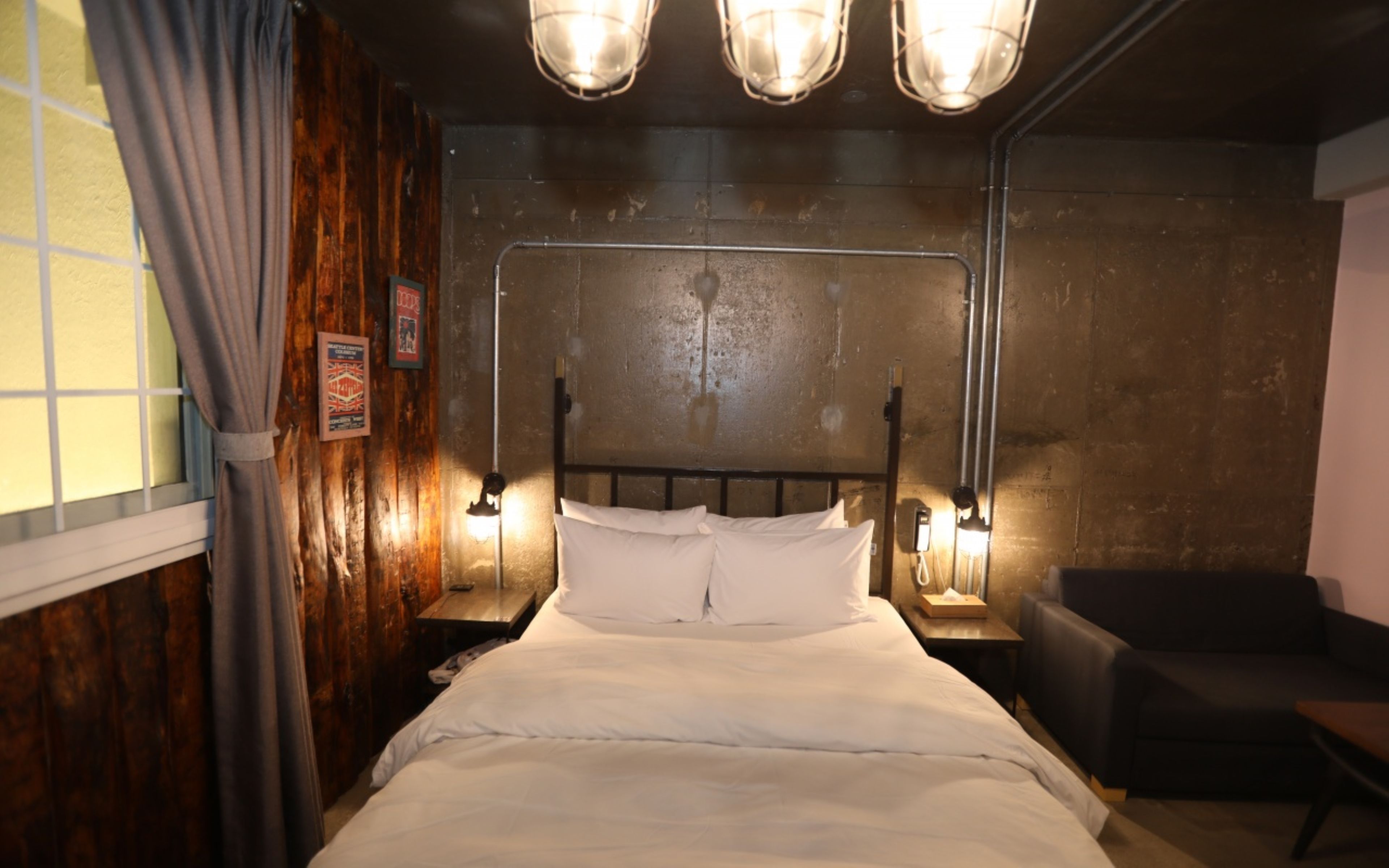 Ein Hotelzimmer mit einem Bett, Nachttischlampen, einem Fenster mit Vorhängen und einem dunkelbraunen Sessel.
