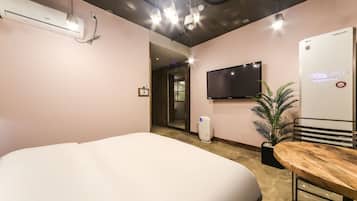A hotel room with a bed, a flat-screen TV mounted on the wall, a small potted plant, and a wall-mounted air conditioner.