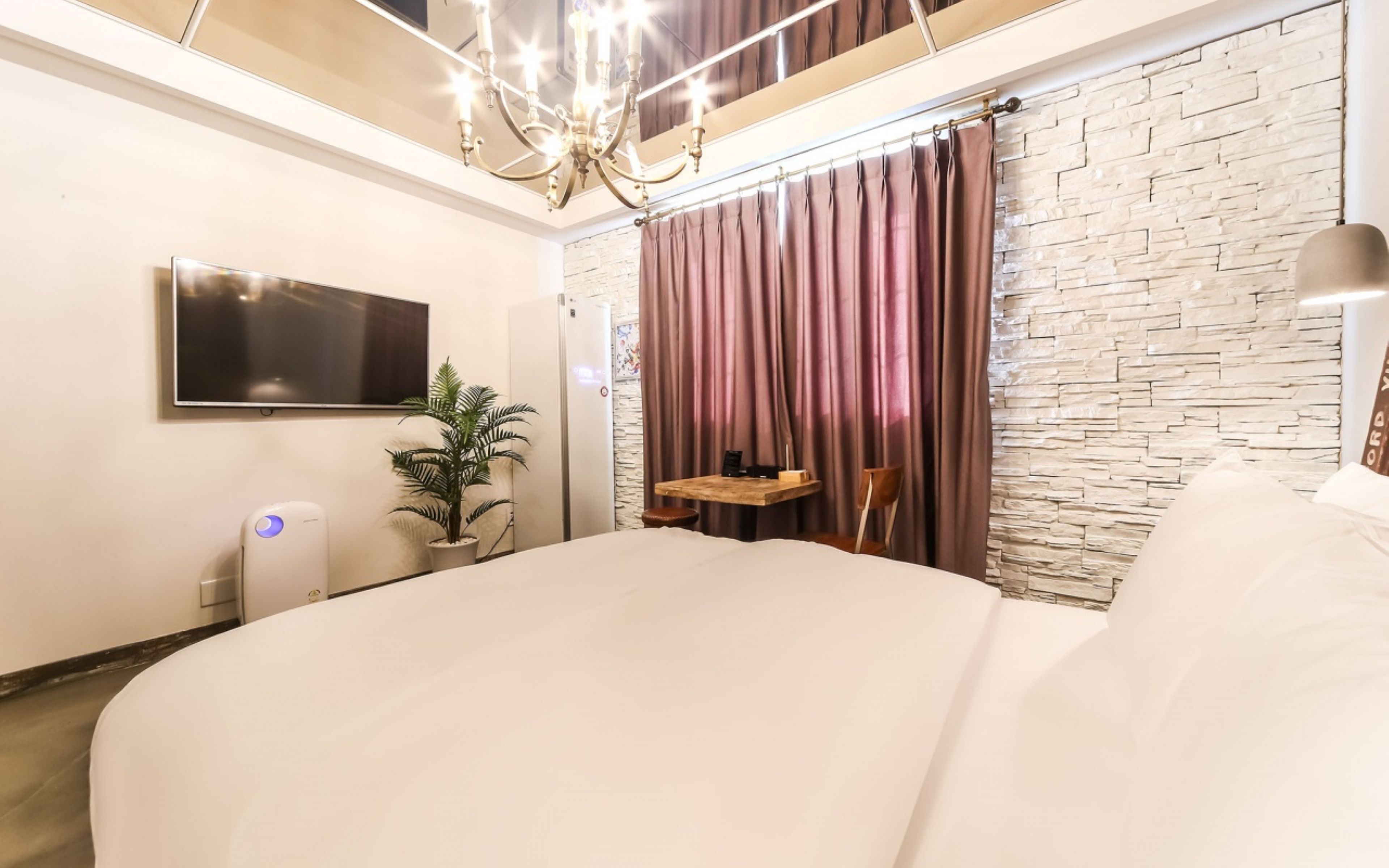 Un dormitorio moderno con una cama grande, un televisor de pantalla plana, una planta en maceta y una pared con textura de piedra.