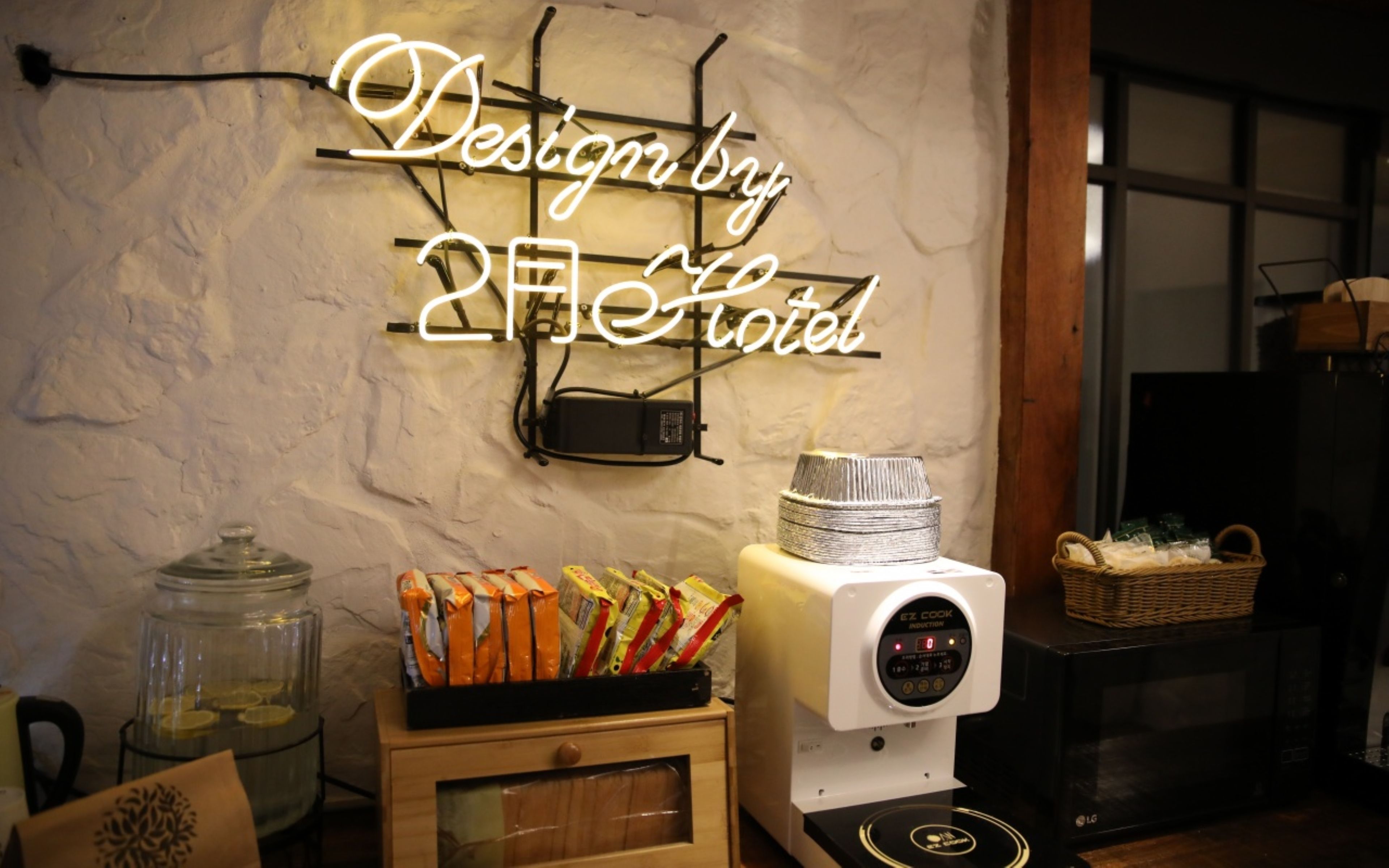 Un área de cocina con un letrero de neón que dice 'Design by 2nd Hotel', una cafetera y una cesta en la encimera.