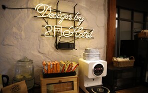Un coin cuisine avec un panneau néon indiquant « Design by 2nd Hotel », une machine à café et un panier posé sur le comptoir.
