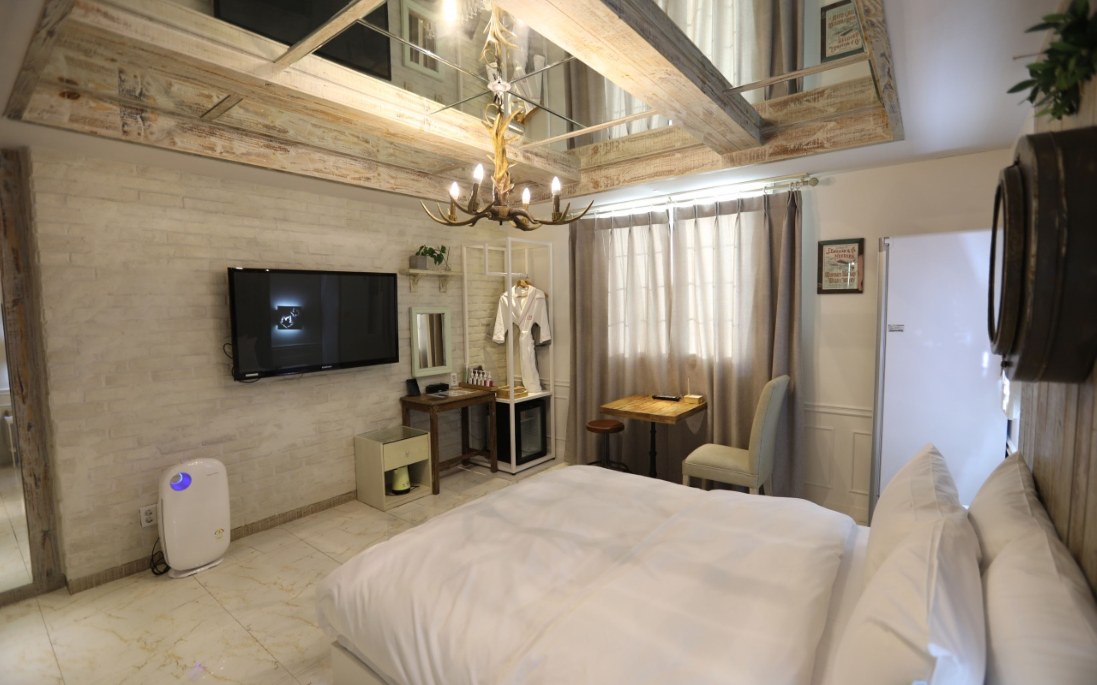 Un dormitorio con una cama grande, un televisor de pantalla plana montado en la pared, un escritorio con una silla, un espejo y un ventilador de techo.