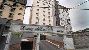 Entrada de um hotel com uma placa indicando "Boutique Hotel 2F" e uma escadaria que leva à entrada.