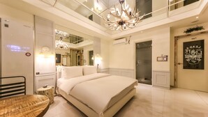 A modern hotel room with a large bed, a chandelier, a mirror, and a door with a sign. - February Hotel - Busan Songdo (Busan)