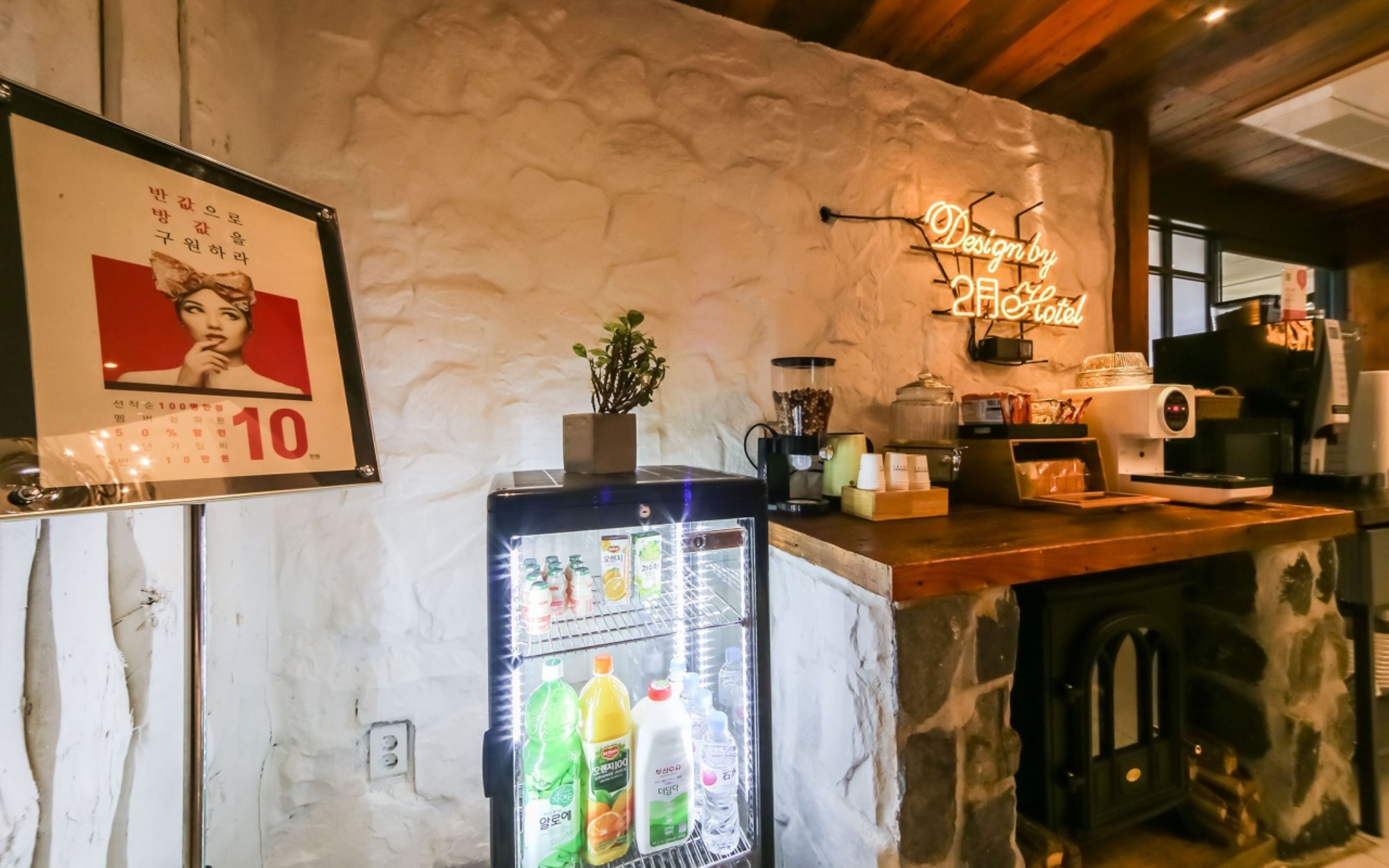 Zona de recepción de un hotel con un refrigerador lleno de bebidas, una máquina de café y un letrero de neón que indica el nombre del hotel.