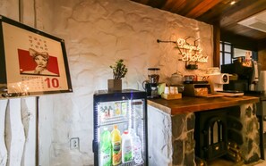 Un espace d’accueil d’hôtel comprenant un réfrigérateur rempli de boissons, une machine à café et un panneau lumineux indiquant le nom de l’hôtel.